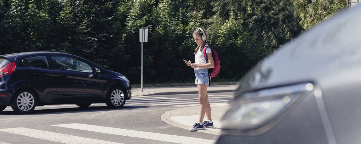 Schoolgirl with headphones and mobile phone on pedestrian crossing